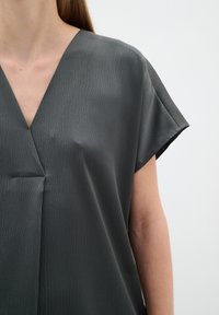 Tricou gri, cu mânecă scurtă și decolteu în V, realizat dintr-un material texturat și având un detaliu subtil de plasare frontală. Material neted, ușor.