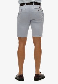 Pantaloni corti azzurri con una vestibilità su misura, tasche posteriori con chiusura a bottone e una vita a contrasto. Indossati con mocassini marroni.
