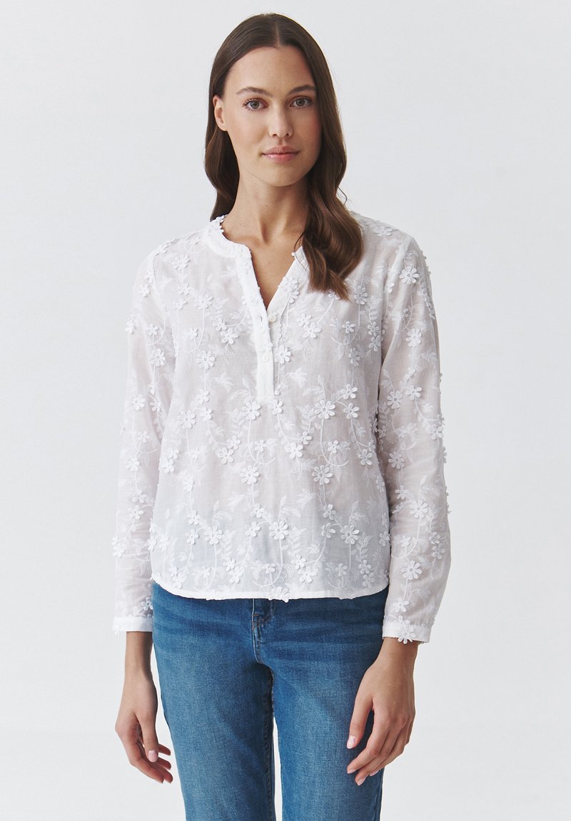 Weiße Baumwollbluse mit floralem Stickerei, Knopfleiste und runder Halslinie. Lange Ärmel und leichtes, leicht transparentes Material.
