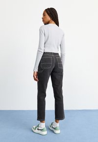 Melnas augstās vidukļa džinsi ar kontrastējošām dzeltenām stīgām un lielām aizmugurējām kabatām. Apvienoti ar gaiši pelēku garām piedurknēm kreklu un sporta apaviem ar zaļiem akcentiem.