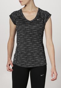 Svart V-inget träningsskjorta med korta ärmar, med ett strukturerat mönster av små vita prickar. Tillsammans med svartaleggings, Nike-logotyp synlig.
