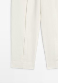 Close-up of the lower part of white straight-leg trousers with a stitched hem on a plain background.