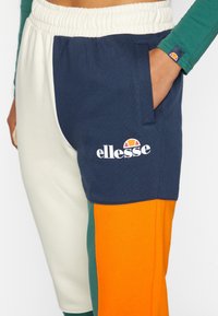 Värikäs collegehousu, jossa on tummansinihattu, kerma-valkoinen ja oranssi väri-blokki design, pehmeä kangas, joustava vyötärö ja sivutasku, jossa on logotyyppi.