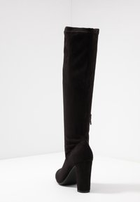 Bottes noires en daim, montantes jusqu'au genou, avec un talon épais, présentant une texture lisse, un design effilé et une fermeture éclair sur le côté pour un enfilage facile.