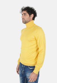 Maglione giallo a collo alto con collo e polsini a coste, design aderente, texture liscia, indossato con jeans blu slavati.