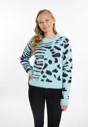 Hellblaues, flauschiges Sweatshirt mit schwarzem Tierprint-Muster, runder Ausschnitt und langen Ärmeln, kombiniert mit schwarzen, eng anliegenden Jeans.
