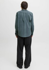 Grønn kordfløyelskjorte med bakre del, avrundet kant og knappeermbånd, kombinert med løstsittende svarte bukser. Jevn tekstur, uformelt design.