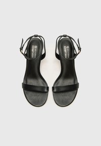 Sandales en cuir vegan noir au design minimaliste. Elles disposent d'une fine lanière à la cheville, d'une large lanière à l'avant et d'une finition lisse et texturée.