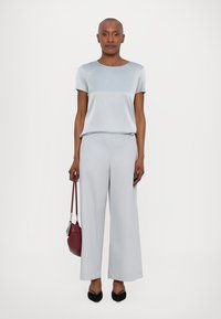 Top de mangas curtas azul claro combinado com calças largas azul claro. O modelo segura uma mala burdeos e usa sapatos pretos de bico fino.