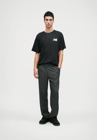 Sort bomulds t-shirt med korte ærmer og hvid grafik. Grå plisserede bukser med lige pasform. Sorte sko fuldender outfittet.