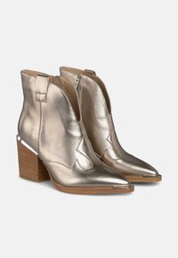 Botas metálicas doradas hasta el tobillo con puntas afiladas, cremalleras laterales y un tacón de madera apilada, con acentos plateados brillantes.