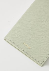 Portafoglio in pelle texture verde chiaro con logo "Furla" in oro stampato. Presenta bordi cuciti, finitura liscia e una forma rettangolare elegante.