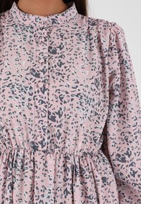 Šaty s leopardím potiskem z jemného růžového materiálu, s vysokým límcem, knoflíkovým zapínáním a elastickým pasem, s nabíranými rukávy a šedými akcenty.