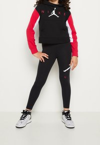 Czarna krótka bluza z kapturem z czerwonymi i białymi rękawami, z kieszenią z przodu i grafiką "NIKE". Czarne legginsy z białym logo. Sneakersy z srebrnymi detalami.