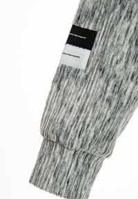 Manga de tela a rayas en gris y blanco con textura acanalada. Se adjuntan dos etiquetas textiles en blanco y negro etiquetadas como "movimiento de onda".