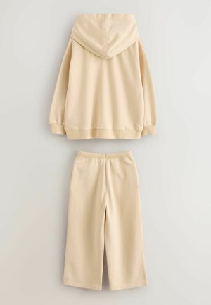 Beige bomullshuvtröja med huva, ribbade ärmslut och matchande avslappnade byxor med elastisk midja och två sidofickor.