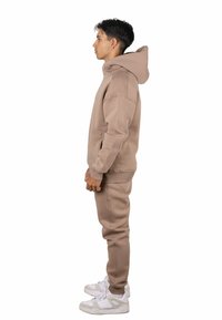 Sudadera con capucha beige y pantalones deportivos a juego confeccionados con tela suave, que cuentan con un bolsillo tipo canguro, puños acanalados y capucha con cordón ajustable.