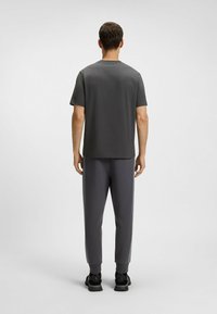 Grå t-shirt med rund hals i kombination med grå snäva sweatpants som har ljusblå sidostripes och svarta träningsskor. Slätt tyg med mjuk textur.