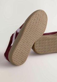 Chaussures en velours bordeaux avec une semelle en caoutchouc beige à motifs et des accents blancs. Le design présente une silhouette basse et des détails texturés.