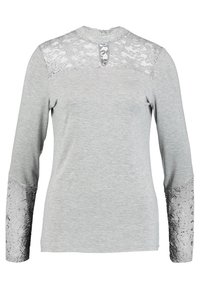 Grå långärmad topp med spetsöverdrag på axlarna och ärmarna. Har rund halsringning och en liten nyckelhålsöppning bak.