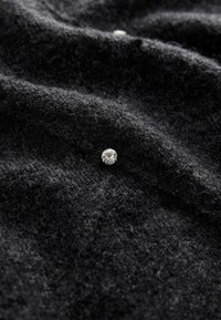 Un petit diamant rond unique posé sur une surface de tissu noir texturé avec des plis doux et des ombres.
