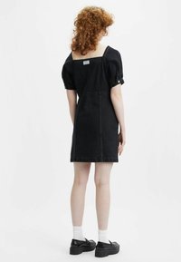 Mustat farkutunika, jossa on neliön muotoinen kaula-aukko ja puffihihat, tiukka vartalo-osa ja hieman levenevä hame. Lyhyt pituus.