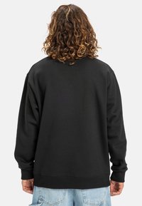 Sudadera negra de cuello redondo con mangas largas, textura suave, corte relajado y puños acanalados. Detalles de costura visibles en la parte posterior.