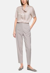 Satin short-sleeve blouse in light beige with a tied neckline, paired with light gray tailored trousers and flat shoes with a decorative accent.
