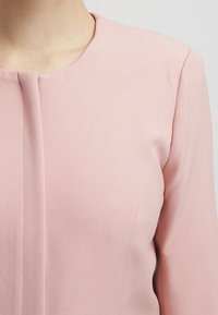 Ljusrosa långärmad topp med rund halsringning, med subtilt texturerad tyg och vertikal sömdetalj fram.