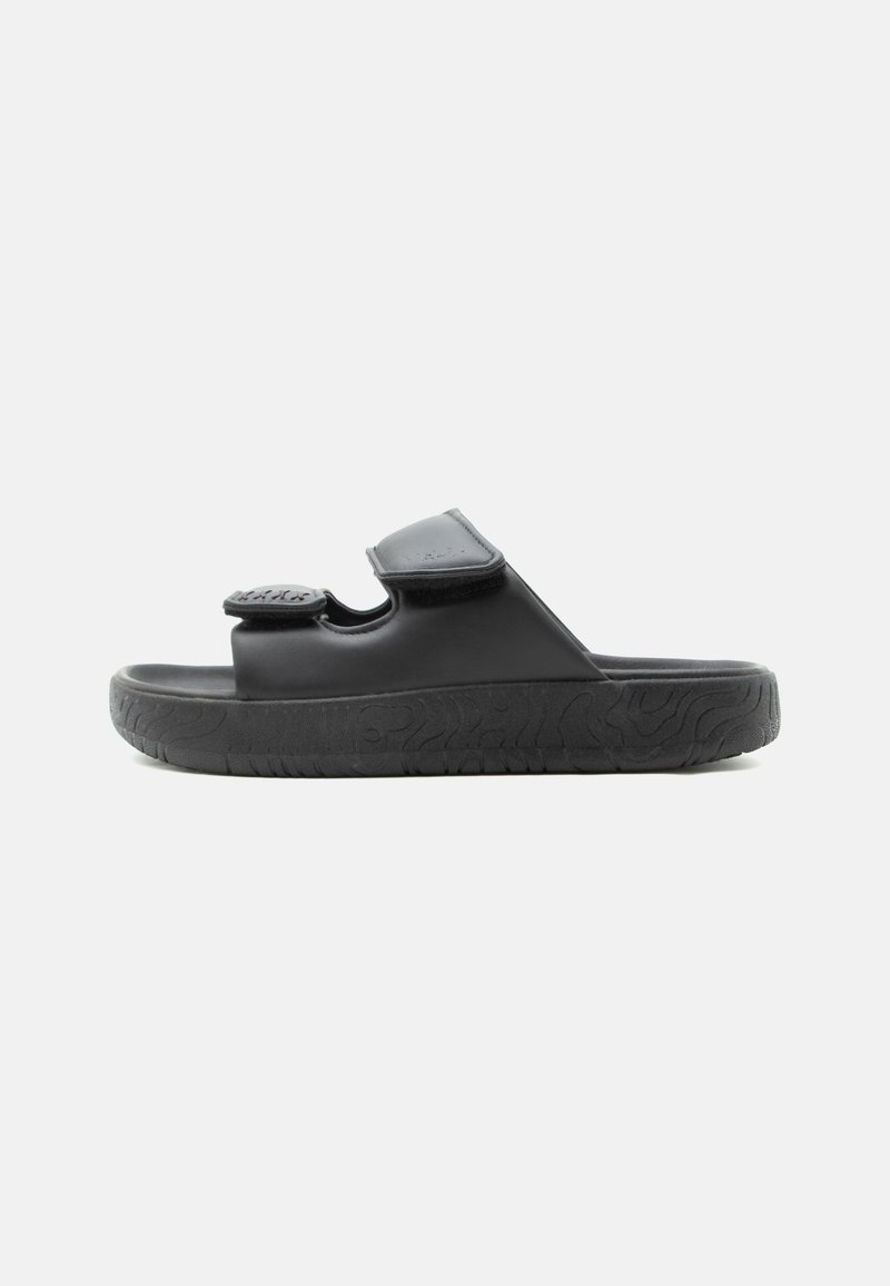 Sandale noire à bout ouvert avec deux brides velcro réglables et semelle texturée, vue de côté sur un fond uni.