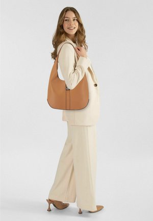 Hellbraune Ledertasche mit rundem Boden und kontrastierendem schwarzen Besatz, mit einem Logo-Akzent und einem einzelnen Schulterriemen.