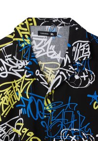 Camicia a maniche corte in tessuto nero con una stampa astratta di graffiti in bianco, blu e giallo. Colletto pieghevole, chiusura frontale con bottoni, etichetta visibile.