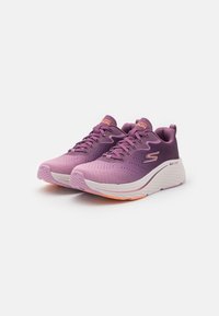 Chaussures de sport violettes avec une tige texturée, un col rembourré et des accents roses contrastés. Elles présentent une semelle blanche épaisse et amortie avec des détails orange.