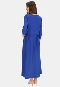 Długa niebieska sukienka z rękawami 3/4, z wcięciem w talii i swobodną spódnicą. Gładki materiał o jednolitym kolorze oraz dekolt w kształcie łódki na plecach.