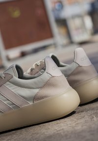 Ljusgrå sneakers med rosa mockadetaljer och tre vita ränder. Har en rundad sula och ett strukturerat läderöverdrag.