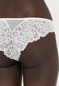 Chiloți din dantelă albi, cu un model floral, detalii din plasă transparentă, margini ondulate și accente cu buline, proiectați pentru confort și ajustare.