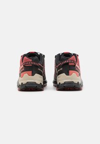 Chaussures de randonnée noires et rouges avec un dessus texturé, dotées d'une semelle rembourrée et d'un renfort au niveau du talon, idéales pour les activités en plein air.