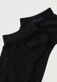 Δύο μαύρες κάλτσες αστραγάλου με ριμπ μανσέτες, η μία με διακριτικό διαμάντι μοτίβο και η άλλη με το λογότυπο "BOSS" κοντά στη μανσέτα.