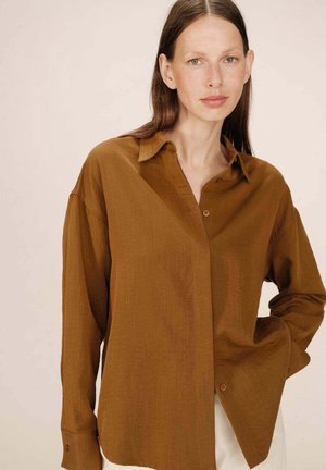 Chemise boutonnée marron avec col, coupe ample, manches longues et texture subtile. Dispose d'un poignet à un seul bouton et d'un design décontracté.