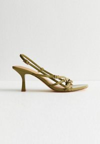 Sandale à talons hauts en olive vert avec des brides croisées, boucle réglable, finition brillante lisse et design à bout pointu.