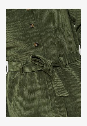 Roheline kangastooted, mille peal on vertikaalsed triibud, ees on nööbid ja vöö. Kangas on pehme ja tekstuuriga.