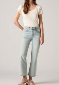 Jeans rectos de color azul claro con cintura alta, bolsillos frontales y un ligero desteñido, combinados con una blusa de manga corta de canal�é color crema.