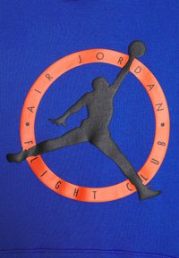 Blauer Sweatshirt mit einer schwarzen Silhouette eines springenden Athleten in einem orangefarbenen Kreis, umgeben von dem Text "AIR JORDAN FLIGHT CLUB" entlang des Randes.