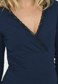 Top de rayas marino con mangas largas y escote en V, que presenta un delicado borde de encaje negro a lo largo del escote, creando un contraste de texturas.