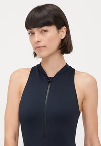 Marinblå zip-up baddräkt med hög halsringning, tillverkad av elastiskt material. Har en slät yta och en central dragkedjedetalj.