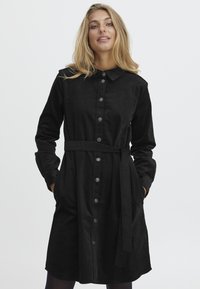 Robe noire à boutons, fabriquée en tissu doux, dotée d'un col, de manches longues, d'une taille ceinturée et de poches. Texture lisse sans motifs visibles.