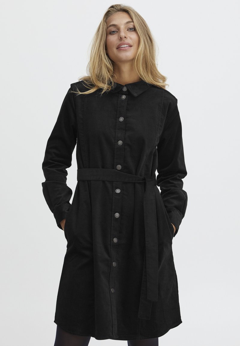 Robe noire à boutons, fabriquée en tissu doux, dotée d'un col, de manches longues, d'une taille ceinturée et de poches. Texture lisse sans motifs visibles.