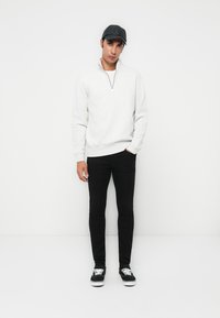 Sweat à zip gris clair, jeans skinny noirs et casquette snapback noire. Baskets noires avec semelle blanche. Tenue simple et décontractée.