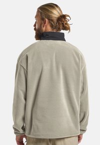 Fleece pullover in light gray with a black collar, features a textured surface and a relaxed fit. The back shows set-in sleeves and a curved hem.