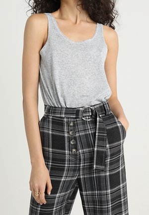 Vrouw draagt een mouwloos grijs gestreept topje dat in hoge taille zwart-witte geruite broek met knopen en riem is gestopt.